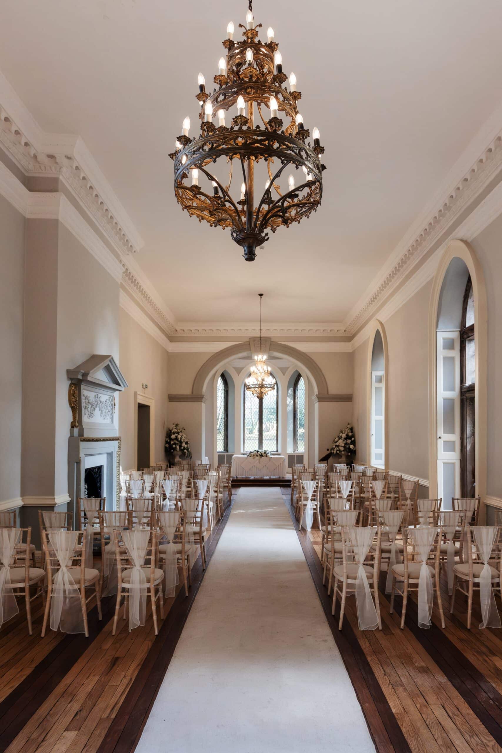 The Ballroom set up for a ceremony at Clearwell Castle, empty aisle and chandelier