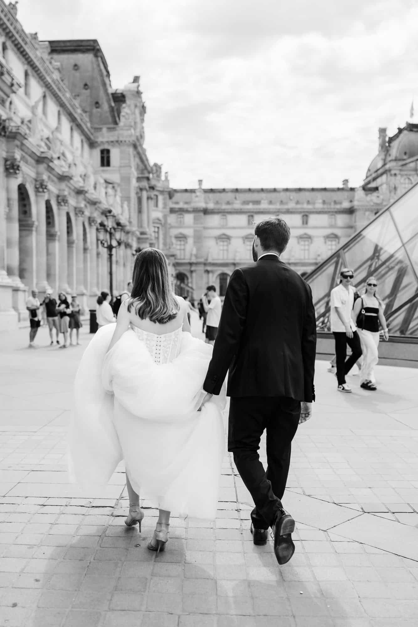 Bride and groom walking through the Louvre colonnade, Paris