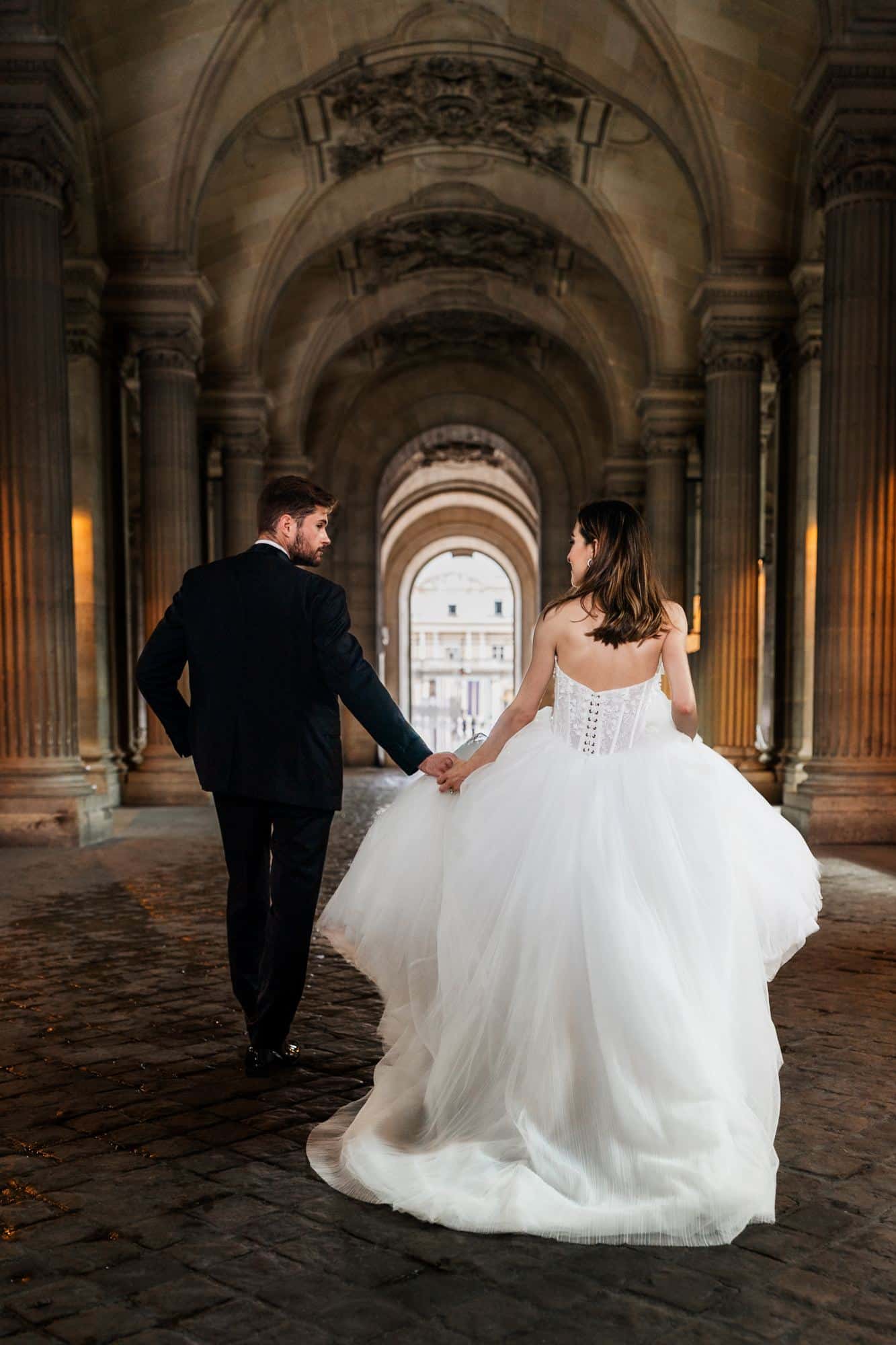 Bride and groom walking through an archway at Palais Royal, Paris